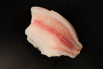Fresh tilapia fillet on black background, top view.
