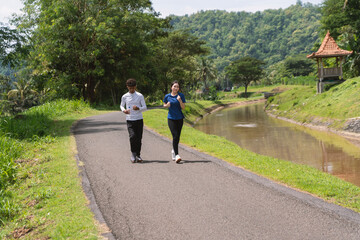 active asian young couple holding water bottle while jogging at rural area