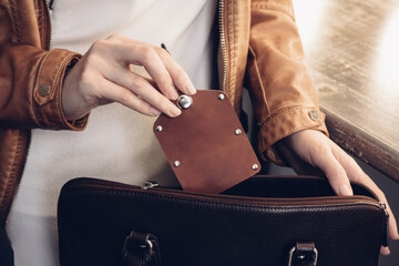 Female hand holding leather keychain pouch above brown handbag