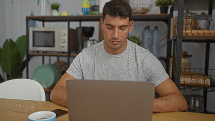 Young man working on laptop in indoor office setting with microwave and plants, showcasing focus...