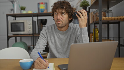 Young man in office listens to voicemail while taking notes, surrounded by modern interior elements...