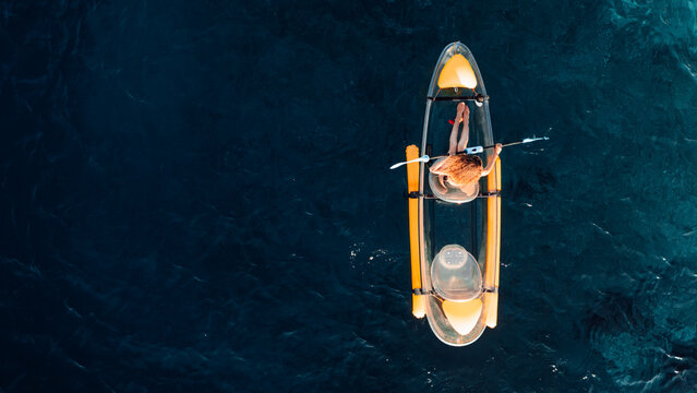Woman float on transparent kayak in blue sea. Drone view, top down