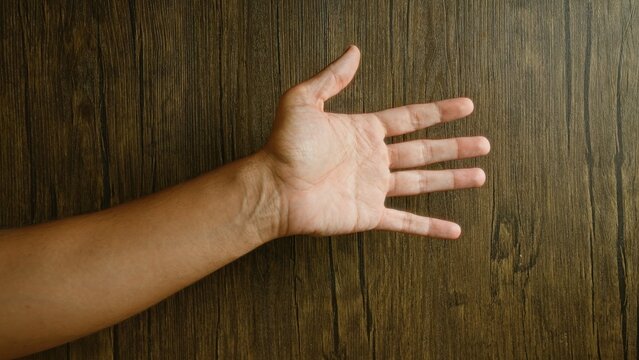 Man hand open with extended fingers against a wooden background showcasing the skin texture and natural wood grain details