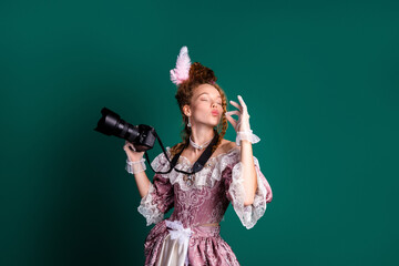Woman in an Elegant Baroque Costume Holding a Modern Camera Against a Green Background