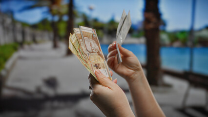 Woman holding peruvian soles outdoors in a sunny urban setting, highlighting travel and business...