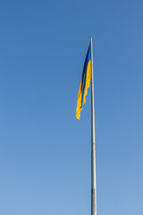 The flag of Ukraine on a high flagpole. The national Ukrainian flag against a clear blue sky. The flag does not flutter, there is no wind