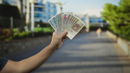 Man holding polish zloty banknotes in hand on city street under sunny sky showcasing currency...
