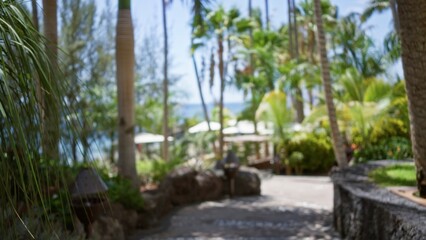 Obraz premium Blurred background of a tropical resort featuring defocused greenery, pathways, and palm trees, capturing a serene, blurry, and bokeh-filled vacation atmosphere.