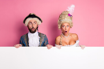 An entertaining couple in retro costumes standing with a blank sign against pink background