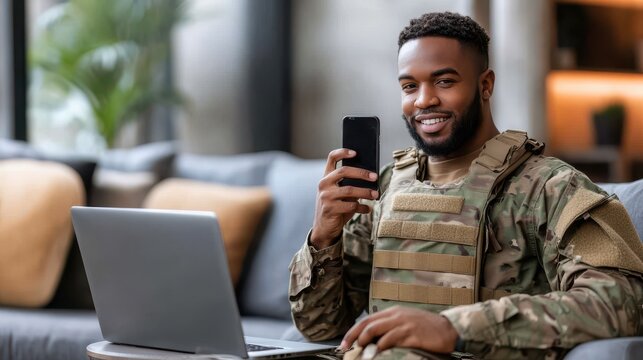 Smiling soldier relaxing at home, using laptop and smartphone