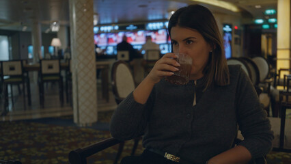 Woman drinking in luxury bar, young hispanic woman enjoying evening indoors, surrounded by elegant decor and ambient lighting, creating a refined and sophisticated atmosphere.