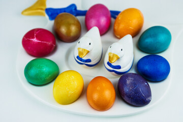 Colorful easter eggs arranged on a white plate with a ceramic duck figurine. Color contrast, creativity, multicolored holiday decoration. Copy space. Selective focus
