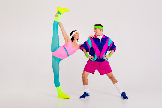 Energetic young couple in vibrant retro workout attire striking playful poses with flexibility on a grey background