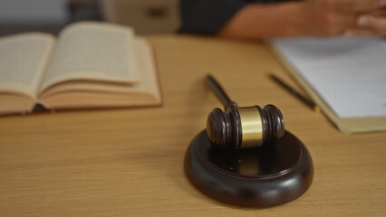 Judge's gavel on a wooden desk in an office with an open book and hands of a young man visible.