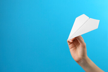 Woman with white paper plane on light blue background, closeup. Space for text