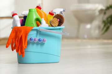 Bucket with different cleaning supplies on floor in bathroom, space for text