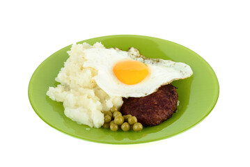 Green plate with cutlet and fried egg and mashed potatoes with green peas on white background.
