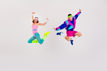 Energetic couple jumping in vibrant retro fitness outfits against a plain white backdrop, capturing a dynamic display of joyful