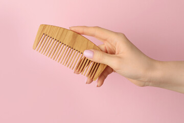 Woman with wooden comb on pink background, closeup. Space for text