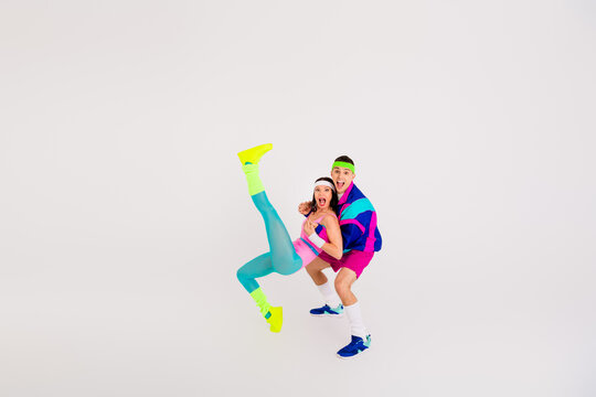 Energetic young couple in vibrant retro activewear performing a dynamic dance pose against a clean white background