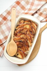 Delicious bread pudding in baking dish and spoon on white wooden table, top view