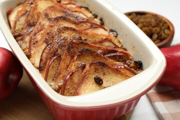 Delicious bread pudding in baking dish and fresh apples on table, closeup