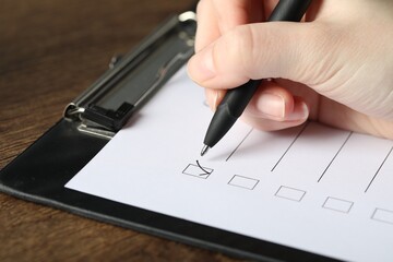 Woman checking box of paper form at wooden table, closeup