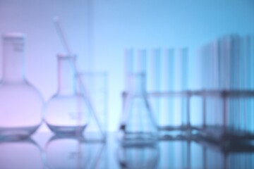Blurred view of laboratory glassware on mirror surface against color background
