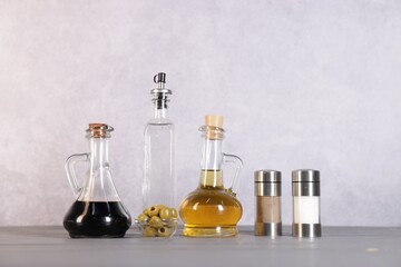 Bottles of salad dressings, salt, pepper and olives on light grey wooden table