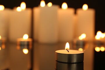 Burning candles on dark mirror surface, closeup. Space for text