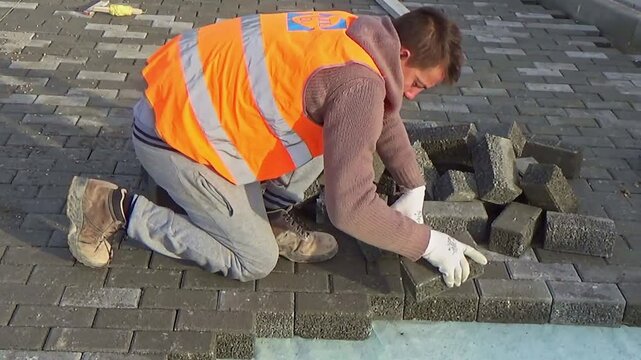 Construction site with workers laying interlocking concrete pavers. Close-up on the installation process, highlighting the precision and teamwork