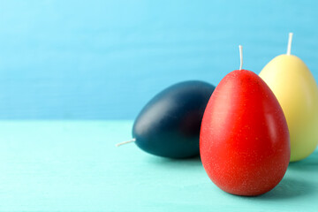Colorful egg-shaped candles on turquoise wooden table against light blue background, closeup and space for text. Easter decor