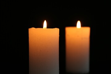 Two burning candles on black background, closeup