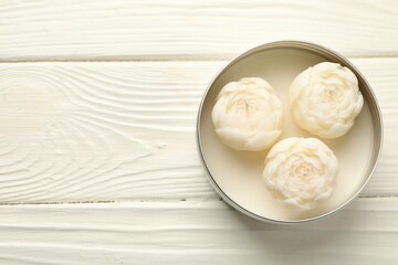 Beautiful flower-shaped candles in jar on white wooden table, top view. Space for text