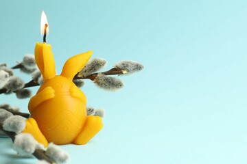 Beautiful burning candle and pussy willow on light blue background, closeup with space for text. Easter decor