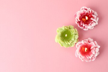 Beautiful burning flower shaped candles on pink background, flat lay. Space for text