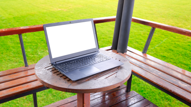 Laptop computer on round wooden desk in gardening area outside of coffee shop, transparent screen with png file 