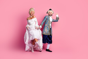 Couple dressed as historical aristocrats posing against a pink backdrop, exuding a lively and festive atmosphere