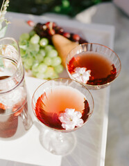 Refreshing cocktails garnished with flowers on a sunny outdoor table filled with fresh fruit