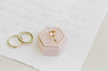 Engagement ring rests elegantly in a velvet box beside wedding bands on a handwritten love letter