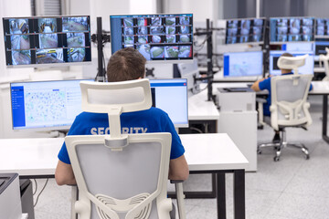 Security officer monitoring multiple surveillance screens in a high-tech control room for safety...