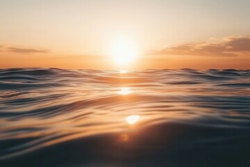 Obraz premium Serene sunset over calm ocean waves, reflecting golden light with soft clouds in the background