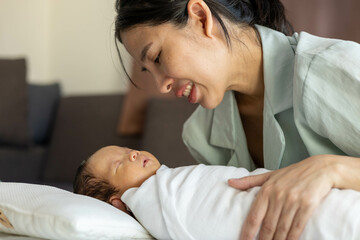 
A woman is holding a baby and kissing its head. The baby is wrapped in a blanket. The woman is smiling and the baby is sleeping
