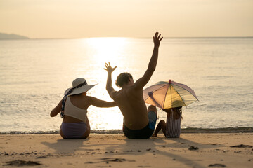 Family enjoying a sunset on the beach with colorful umbrella and hats while creating lasting...