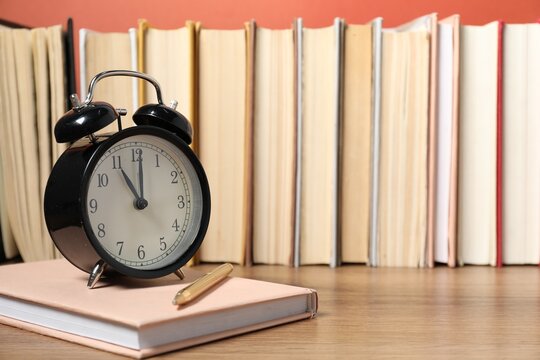 Alarm clock, books and pen on wooden table, space for text. Time for knowledge