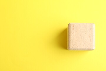 One wooden cube on yellow background, top view. Space for text