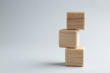 Stack of wooden cubes on light grey background, closeup. Space for text