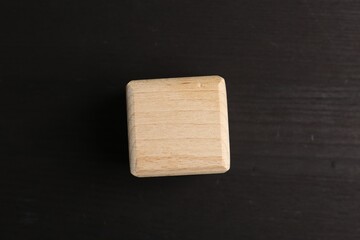 One blank wooden cube on black table, top view