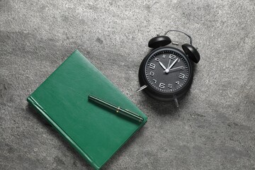 Time for knowledge. Alarm clock, notebook and pen on grey textured table, flat lay