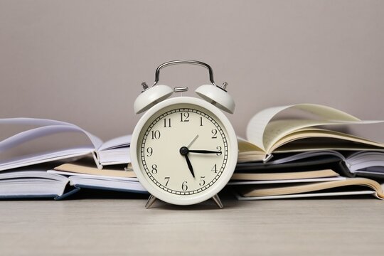 Time for knowledge. Alarm clock and open books on white wooden table - Powered by Adobe